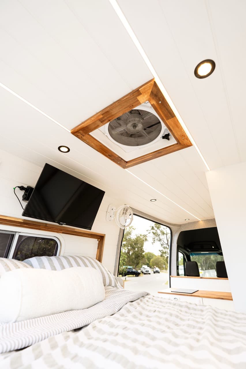 Fixed bed with a wall-mounted TV and a timber-framed roof fan above it