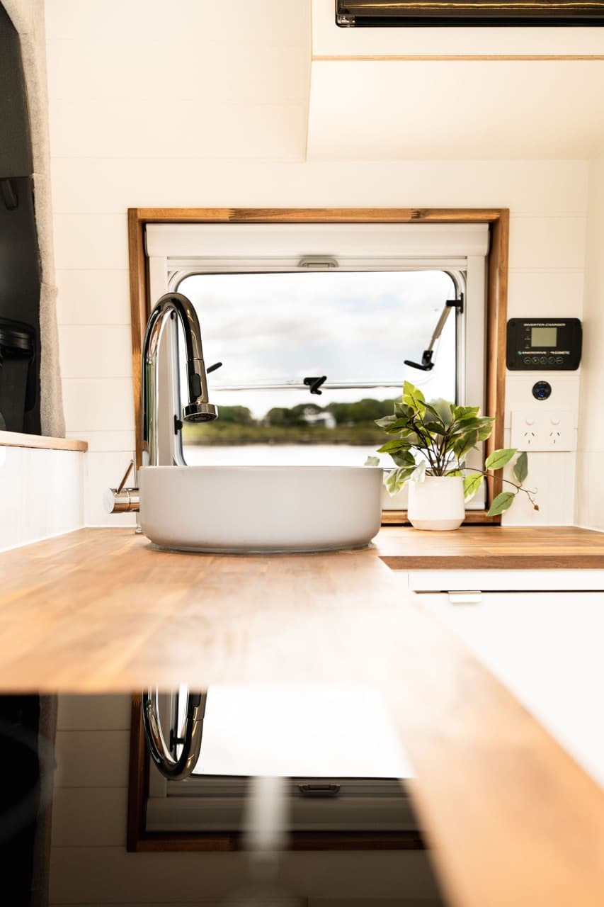 Round basin and tapware set into a timber benchtop beside a van window