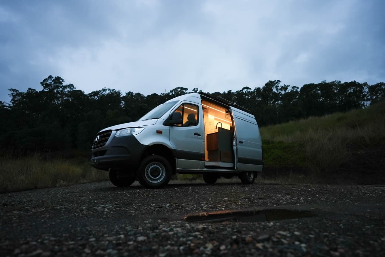 Tim & Lin’s campervan at dusk with the side door open and the lights on